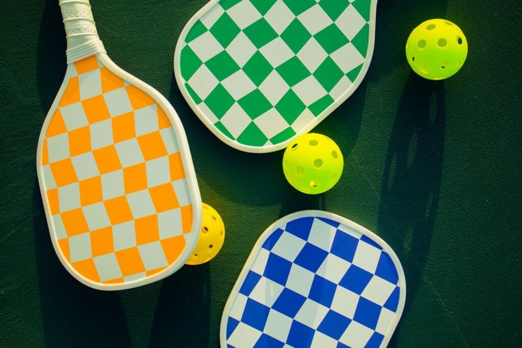 pexels-photo-19642658 Vibrant pickleball paddles and balls arranged on a sunny sports court.